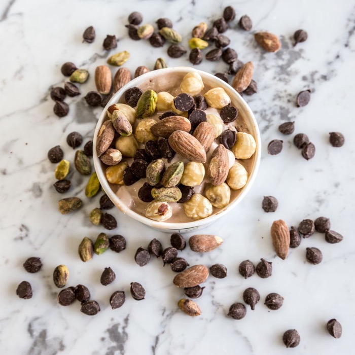 Bowl of mixed nuts and dark chocolate on white marble