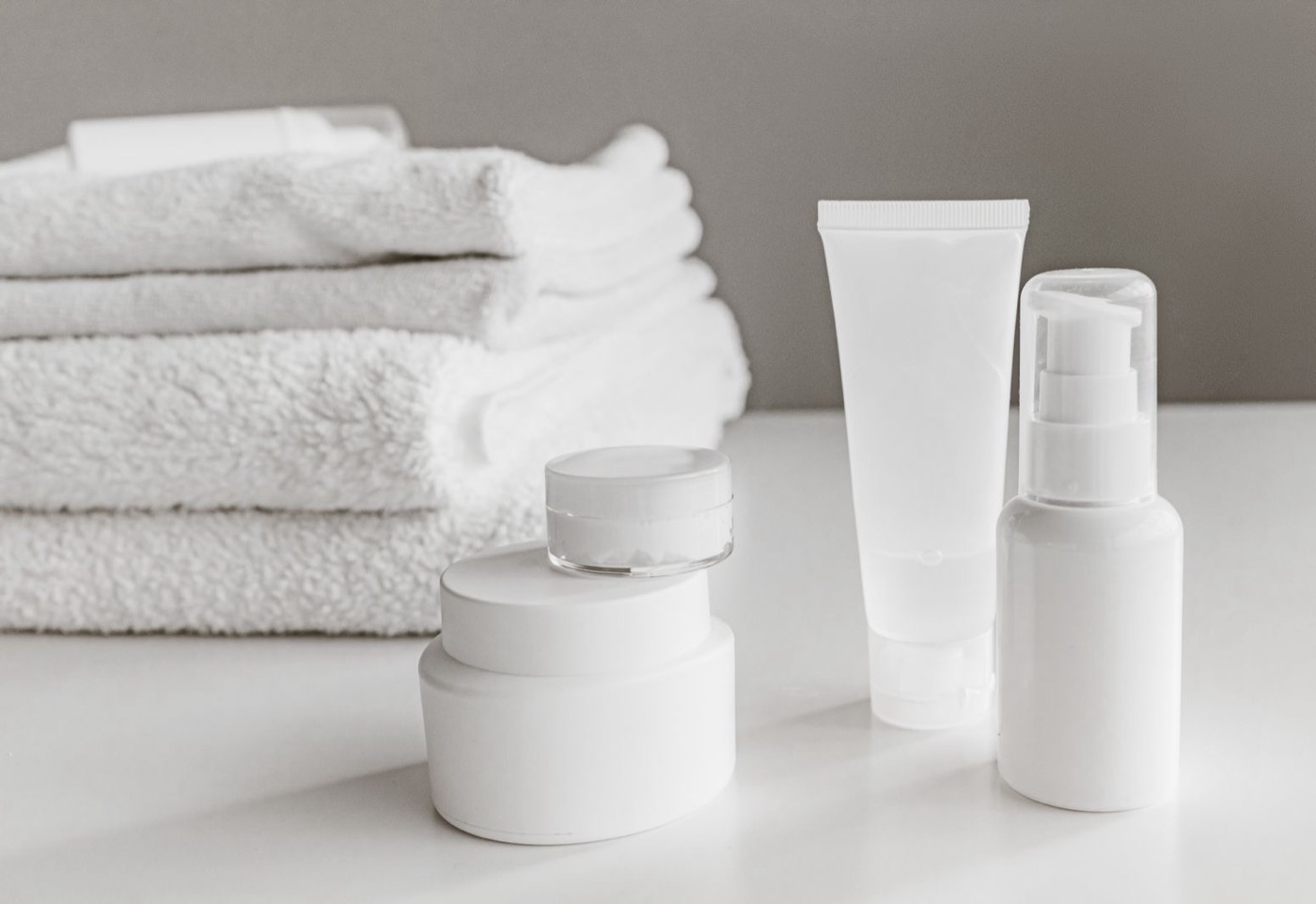 Minimalist white skincare bottles and jars styled beside folded towels
